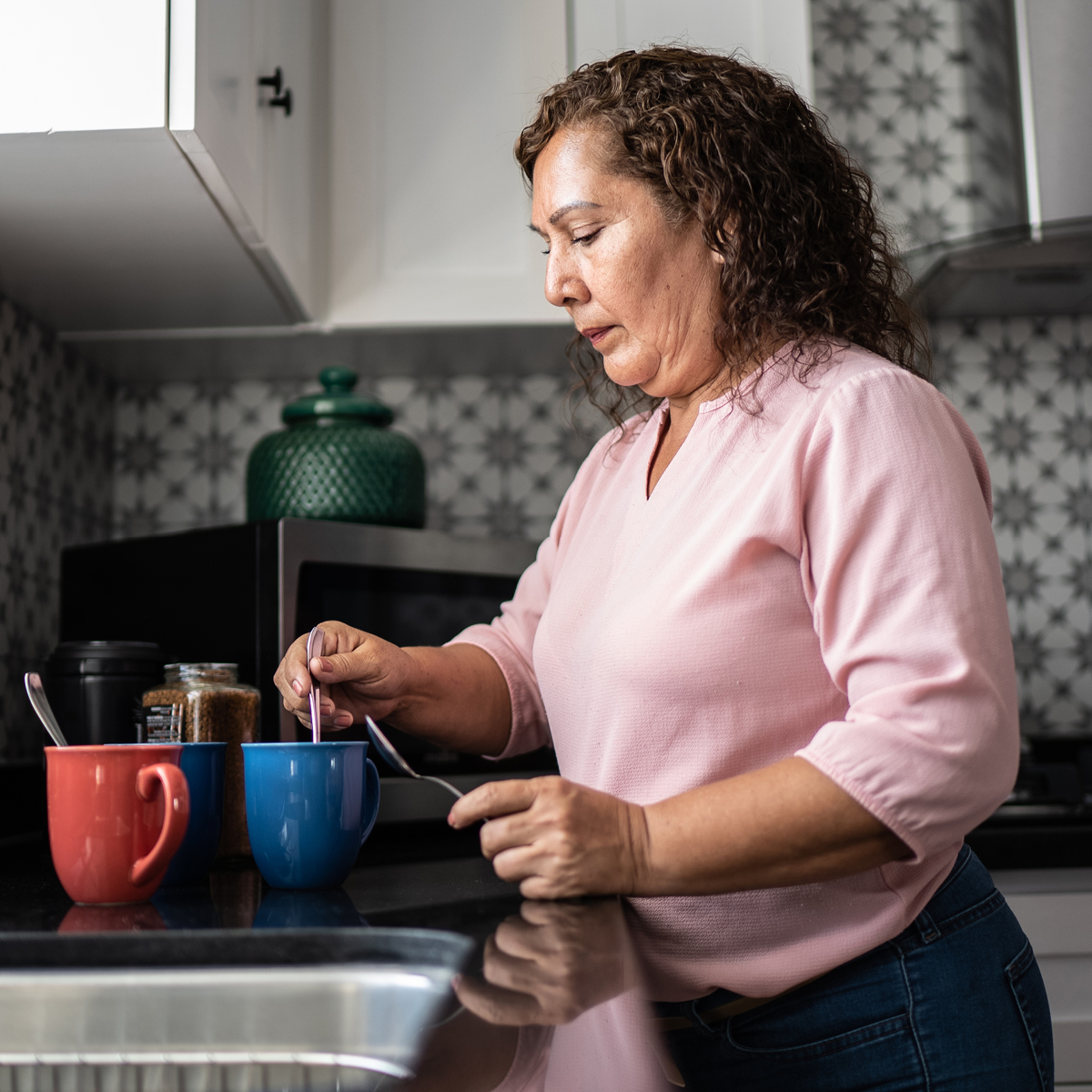A man and woman are in a modern kitchen, preparing food and drinks together in a relaxed, home setting.