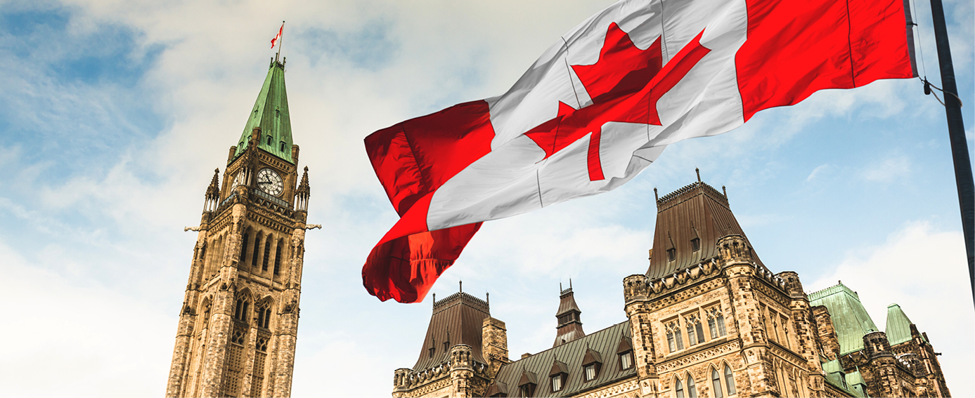 The Canadian government's flag majestically flies against the blue sky over a European city's architectural tower.