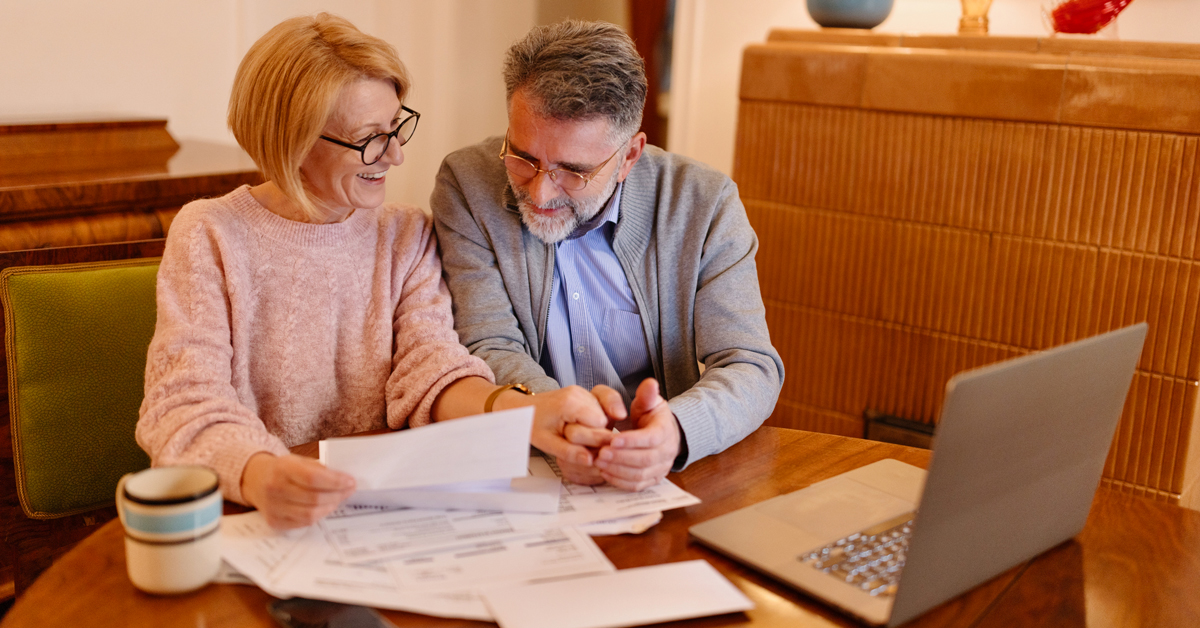 Smiling mature couple reviewing documents with laptop open at kitchen table