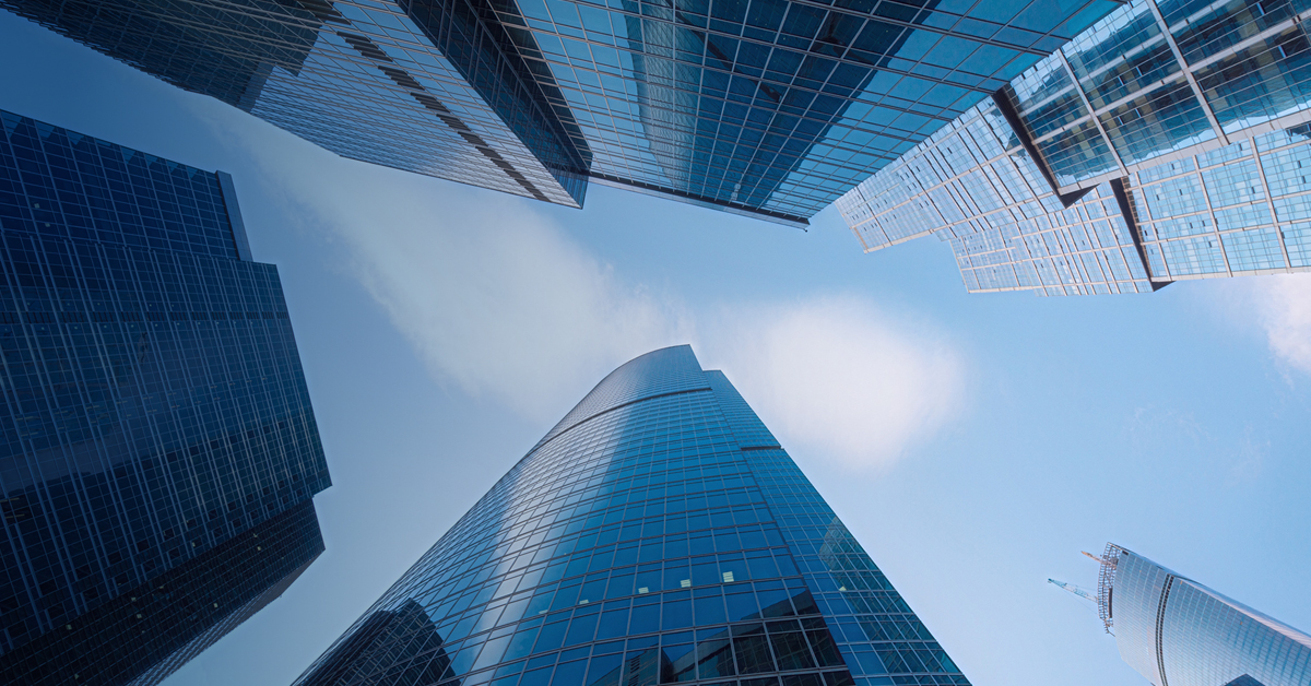 A modern skyscraper with sleek glass architecture reflects the blue sky, showcasing contemporary urban office design.