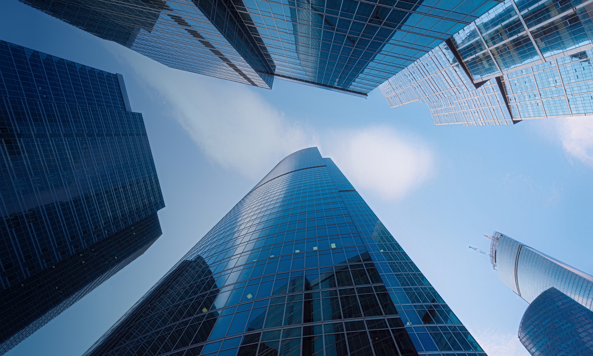 A modern glass skyscraper reflects the blue sky, showcasing sleek architecture in a bustling city business district.