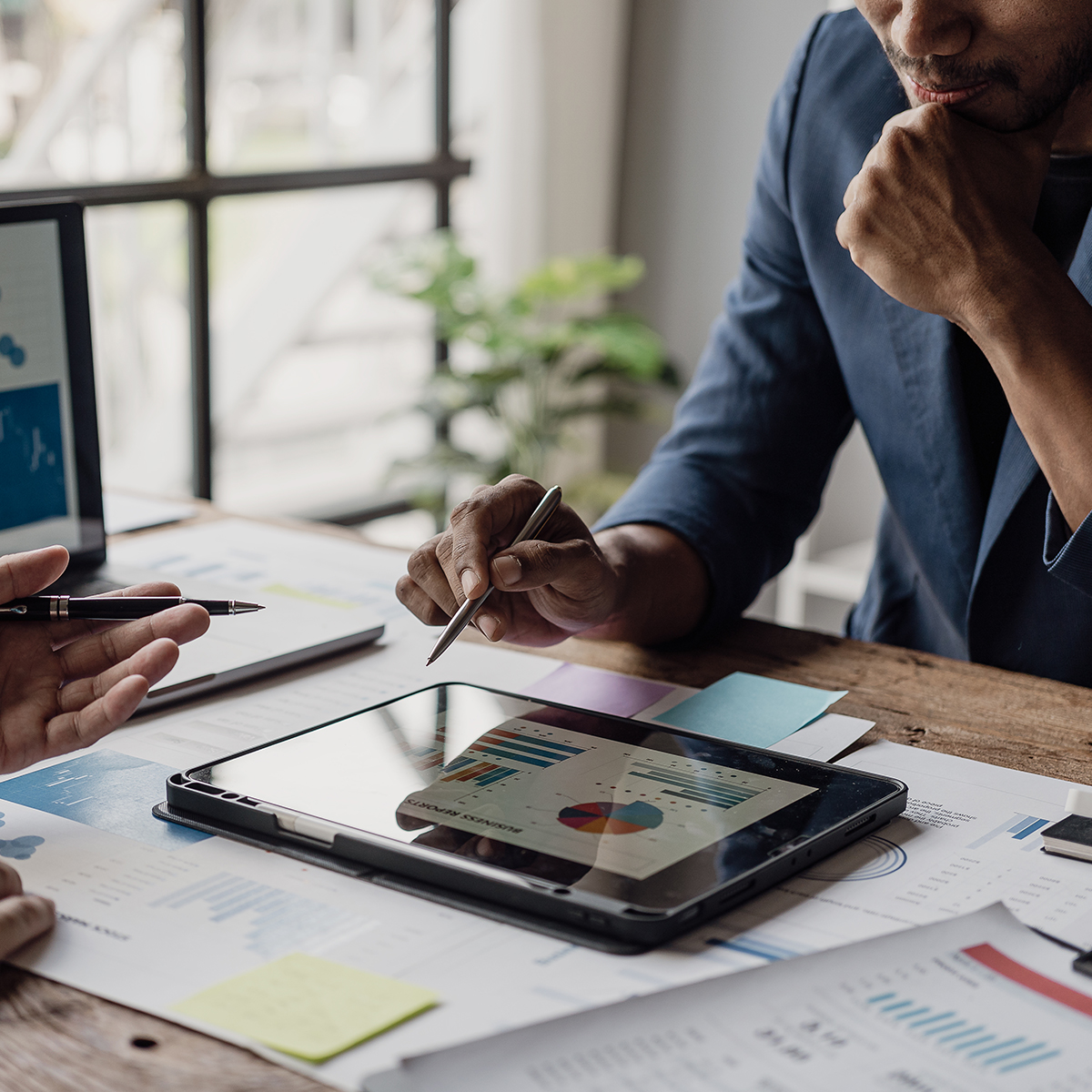A businessman and businesswoman in formal attire review a document together in a professional office setting.