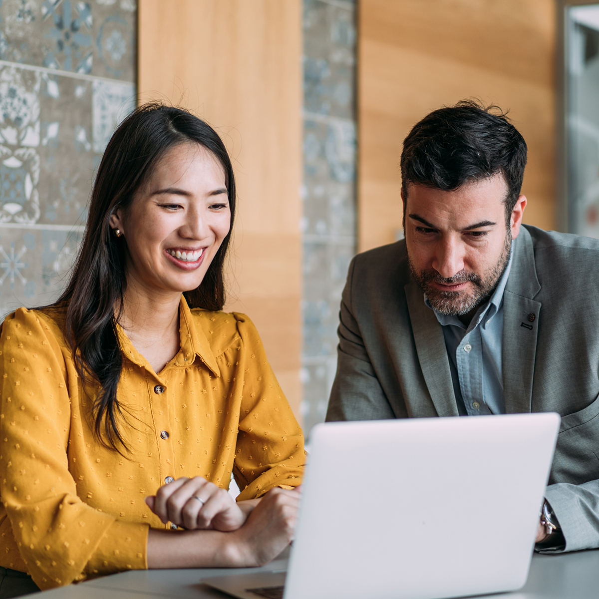 A professional couple works together on a laptop, smiling as they collaborate on a business project using the internet.