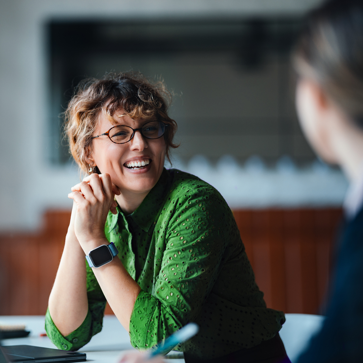 Business photography of a call-center woman presenting to a client at a square table, laughing during the meeting.