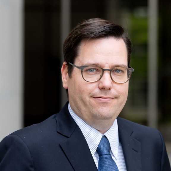 Square business headshot of a man with a tapered haircut, facing forward, prepared for a corporate client speech.