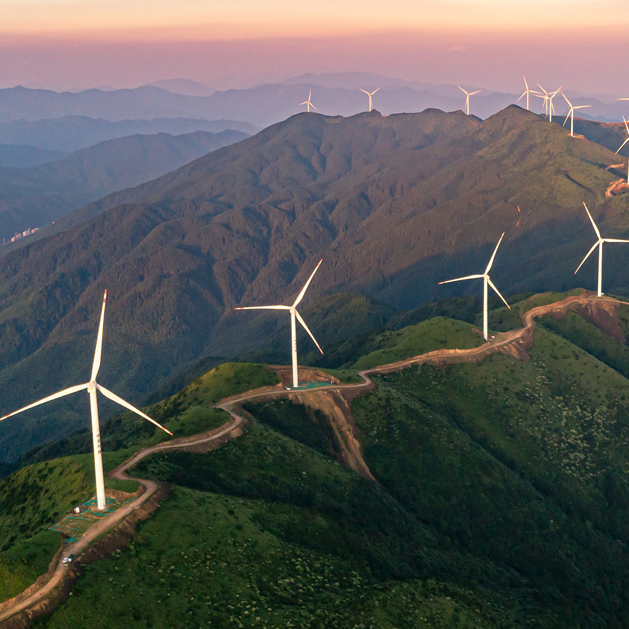 Wind energy turbines dot the landscape, harmoniously blending power and nature against a stunning blue mountain sky.