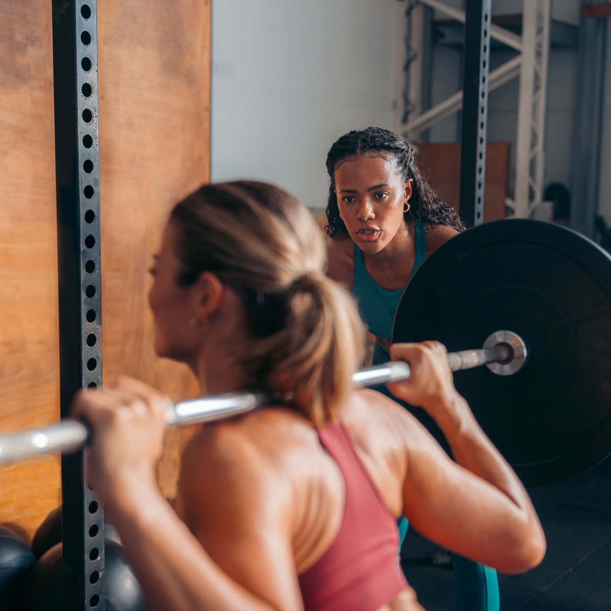 People in a square gym layout perform barbell circuit training, demonstrating strength and weightlifting with a coach.