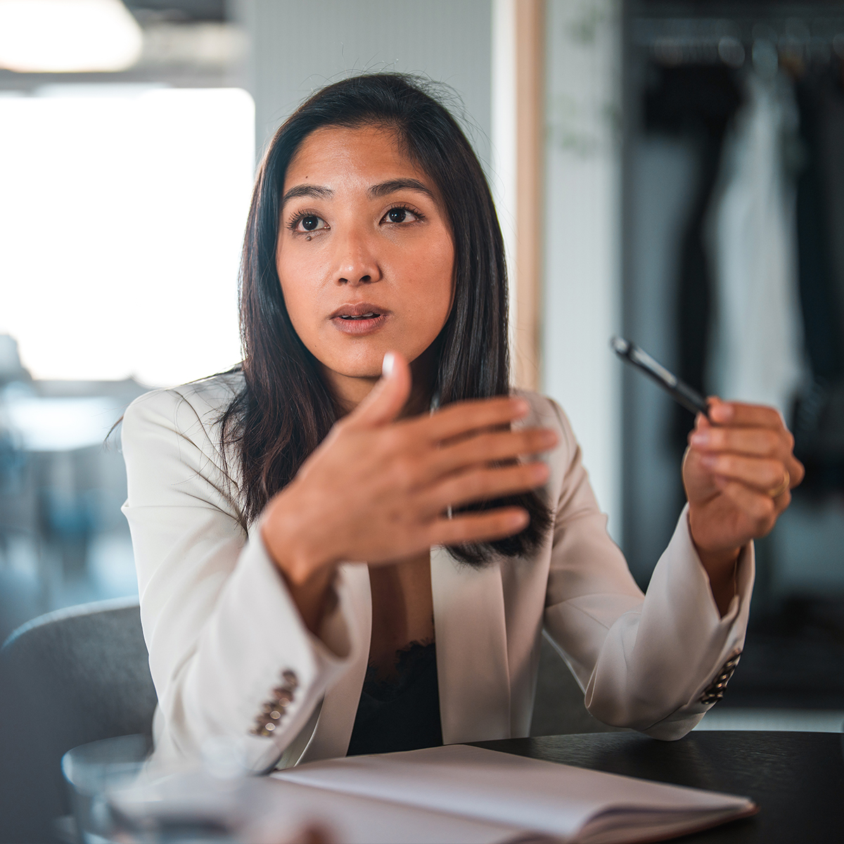 Person gesturing with one hand and holding a pen in the other, appearing to explain or discuss something.