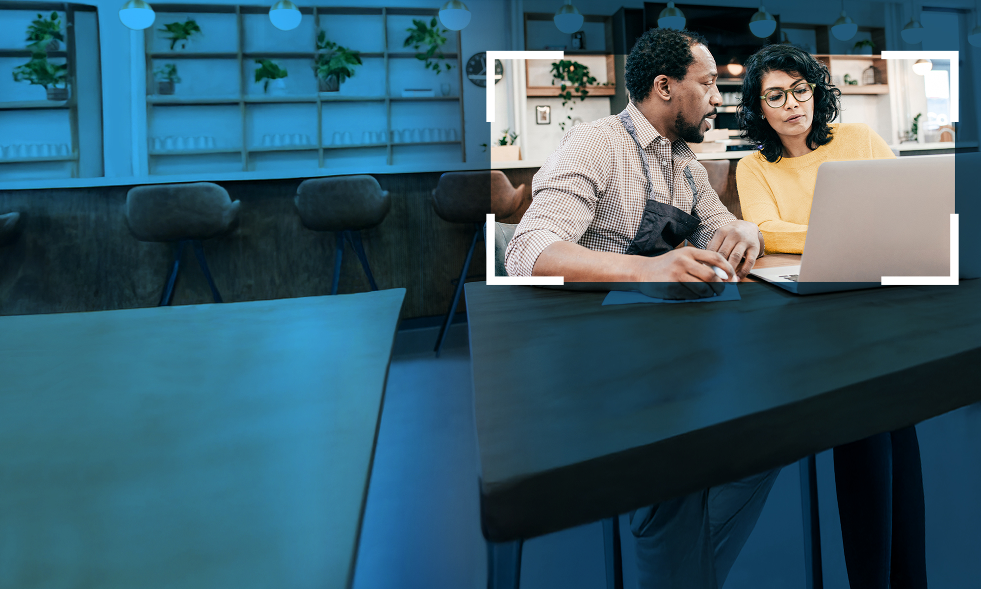 Two people sitting at a table with a laptop, engaged in a discussion in a home-like setting.