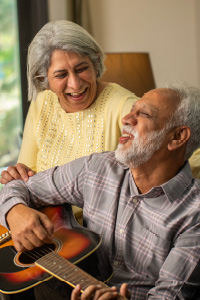 An elderly couple smiles warmly at home, showcasing a happy and comfortable moment in their senior years together.