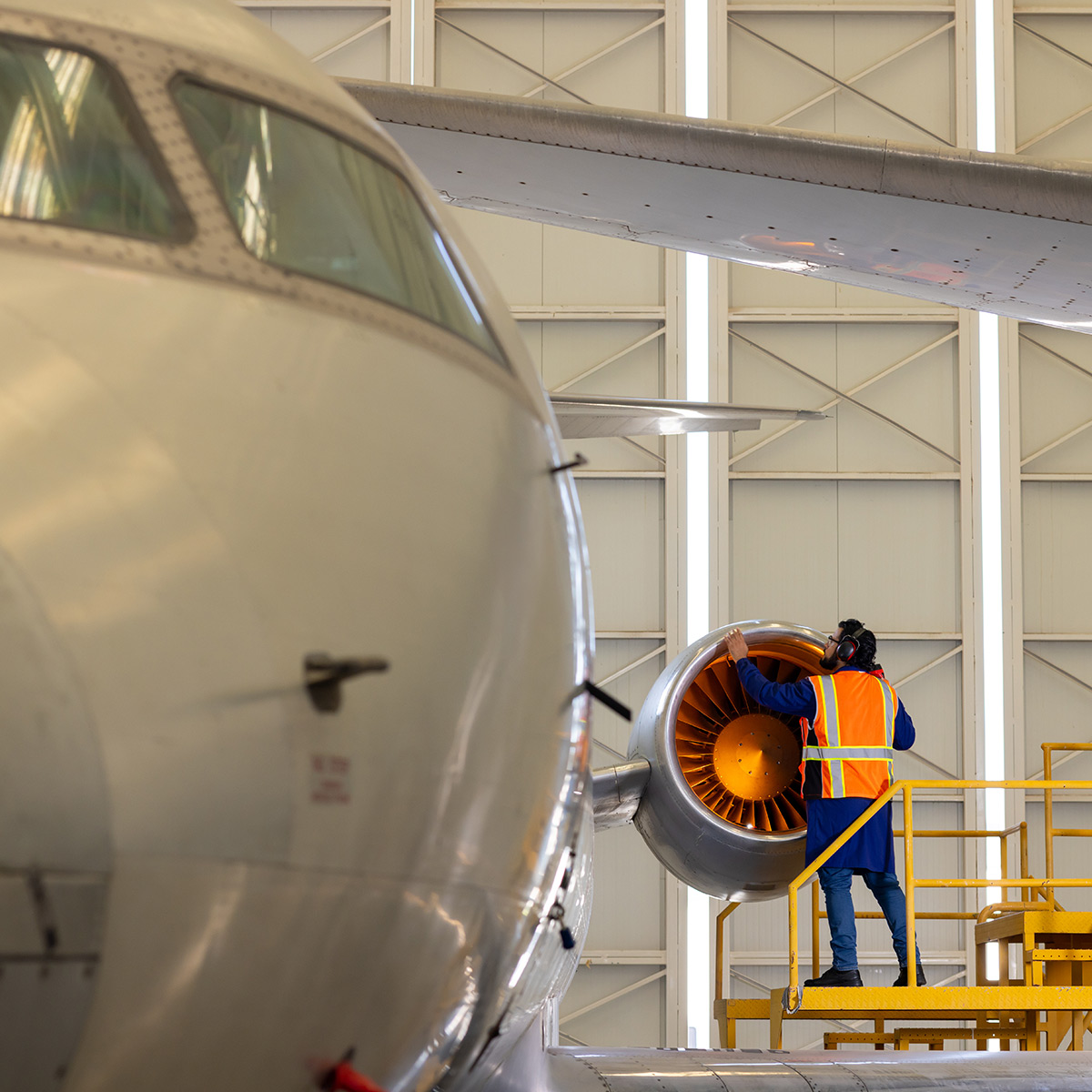 Technician inspects a jet engine near the aircraft fuselage in a hangar, relevant to aerospace engineering and airlift.