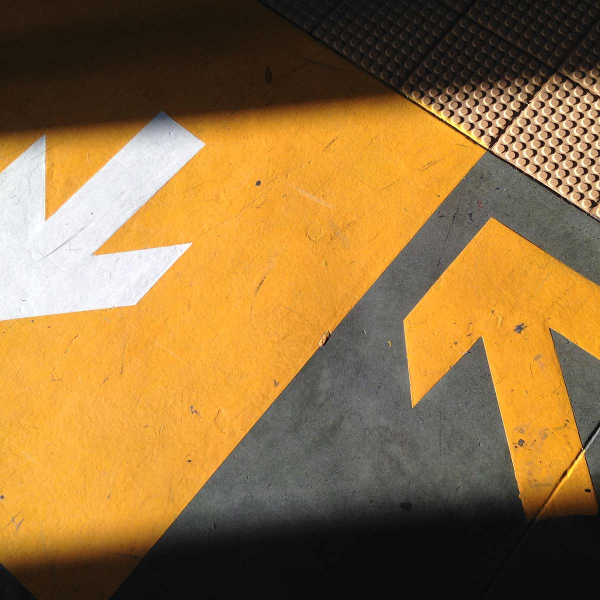 The image depicts a black arrow symbol on a yellow sign, placed strategically on an asphalt road, directing street traffic.