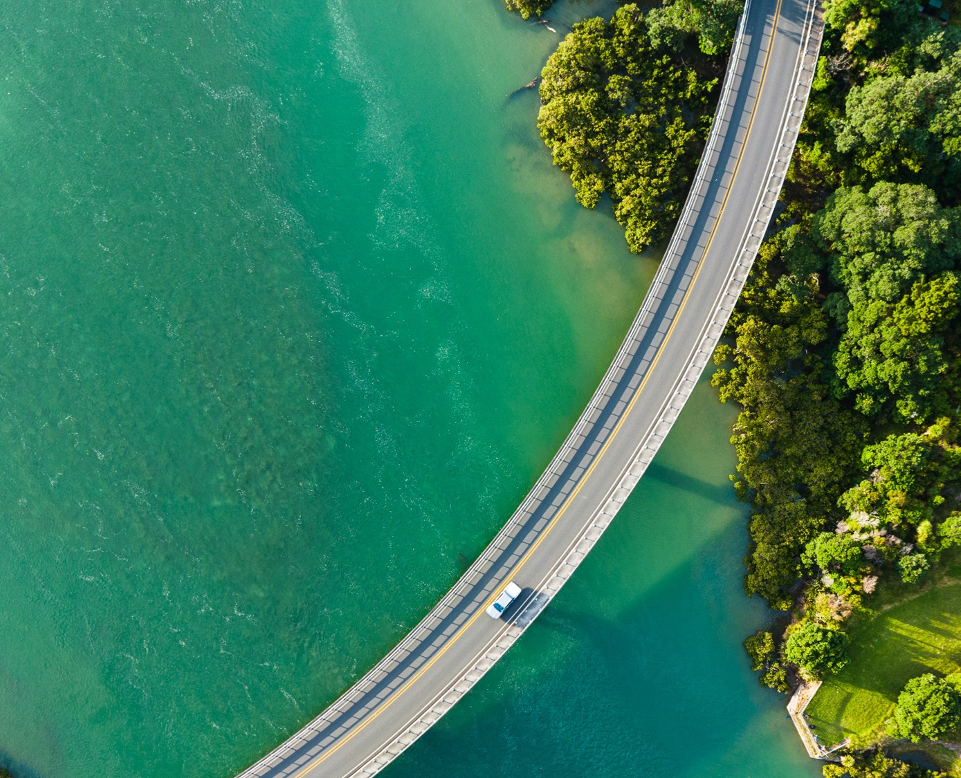 Aerial view shows a winding thruway and suspension bridge over a coastal inlet, showcasing area infrastructure and terrain.