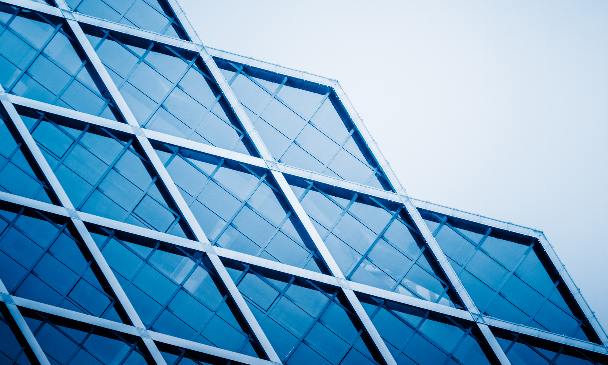 A modern glass office building reflects the clear blue sky, highlighting contemporary design in a vibrant urban business hub.