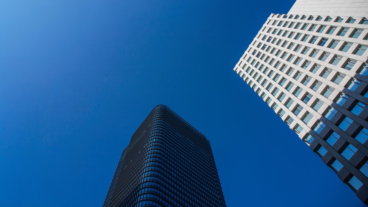 A modern glass skyscraper with a blue-tinted facade stands against a clear city sky, showcasing modern office architecture.