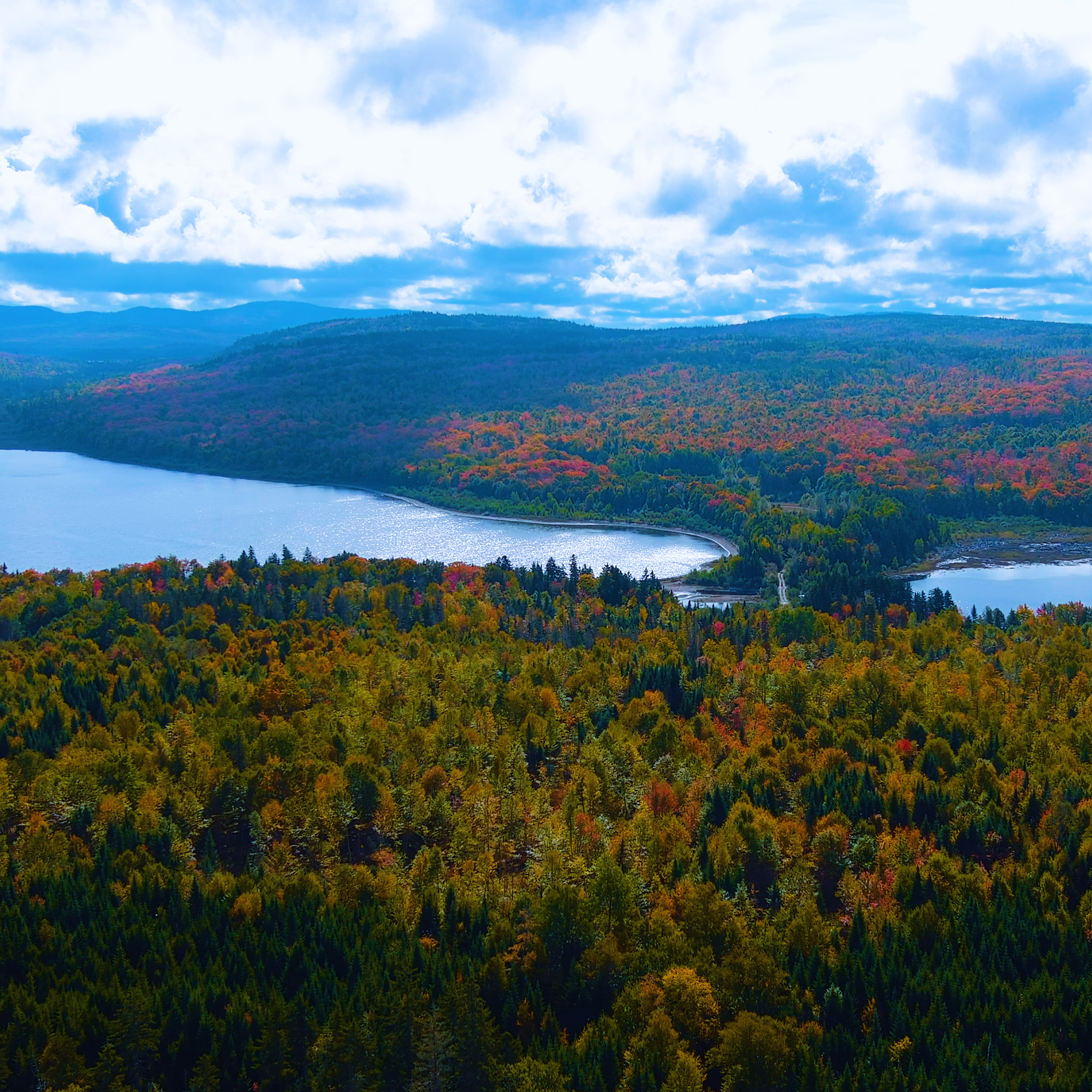 A tranquil landscape featuring rolling green hills, lush forests, and towering mountains beneath an autumn sky with soft clouds.
