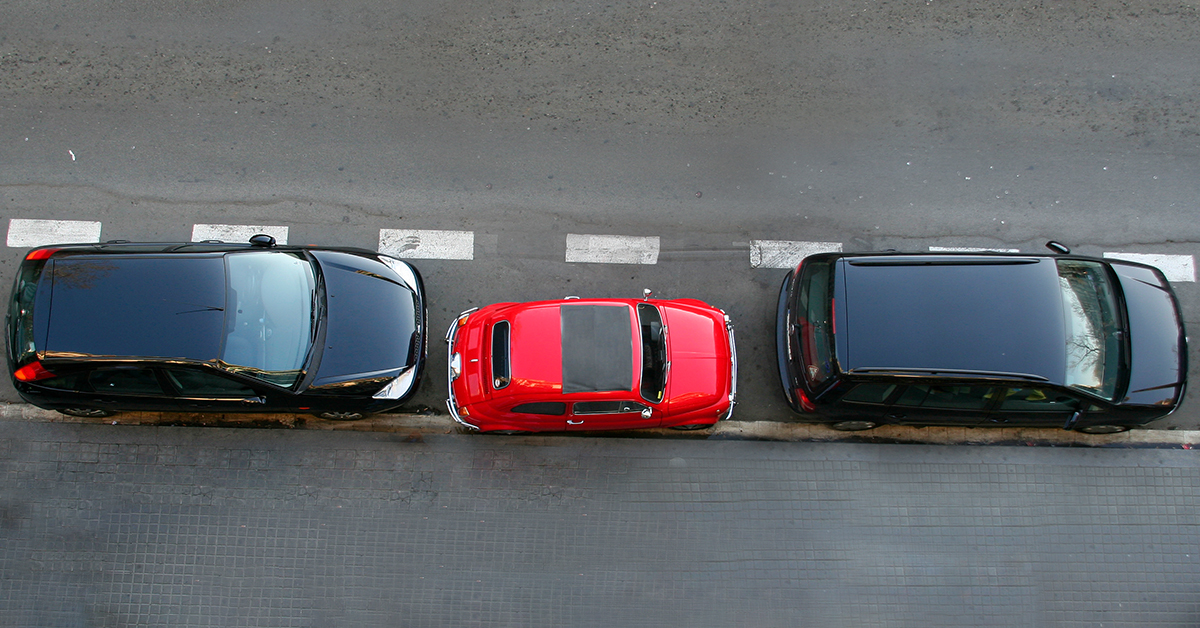 Ariel image of two black SUV's on a road, with a small red car squeezed in between them