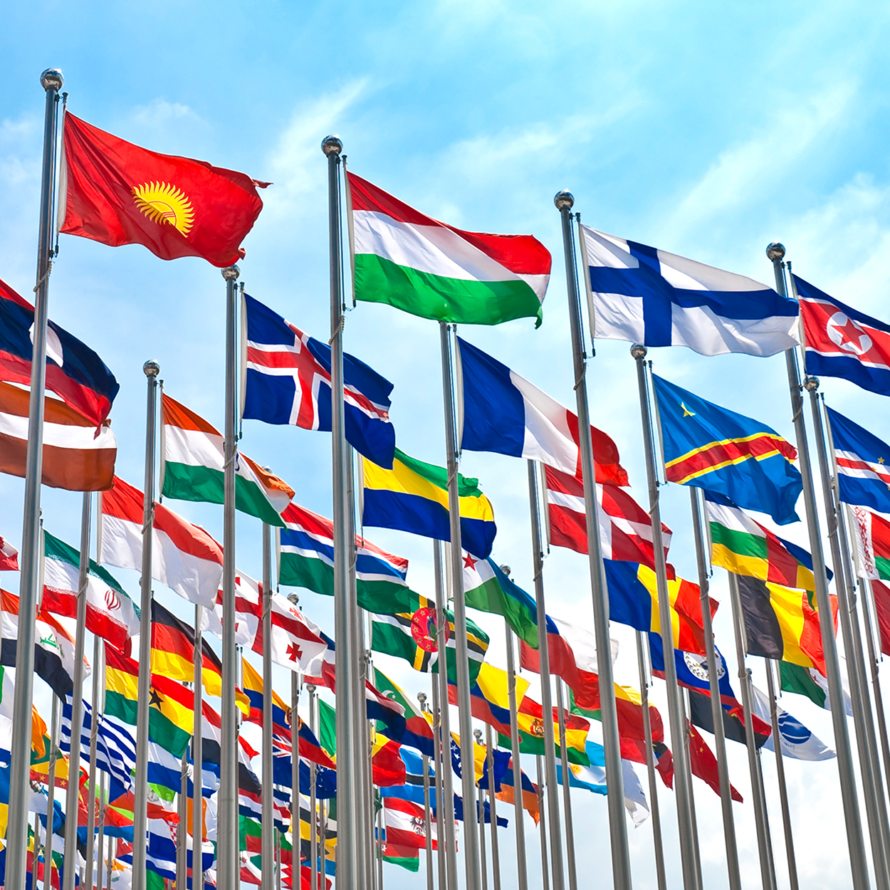 Les drapeaux nationaux de divers pays, symbolisant l'unité mondiale, flottent fièrement sous un ciel bleu.