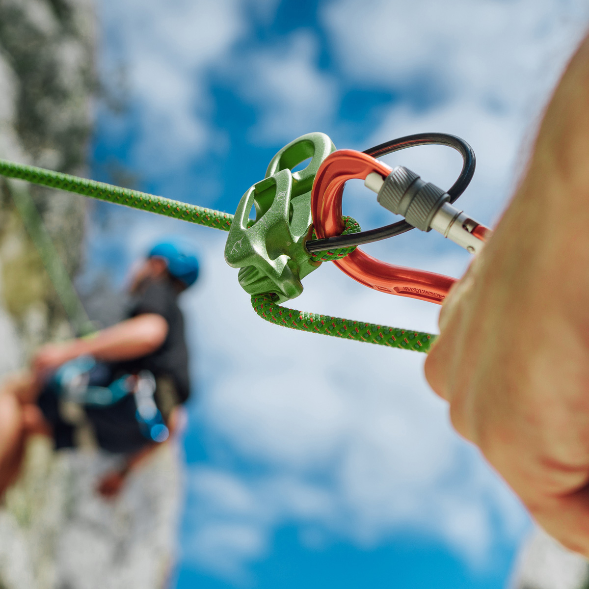Square sports photograph of a male mountaineer rock climbing with a trekking pole and bungee attachment for stability.